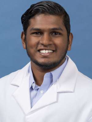 White coat head shot of Roshan Srinivas Srinivasan, smiling at the camera