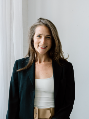 Woman by window wearing dark blazer and white top