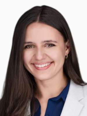 Smiling woman in white blazer and navy blouse against plain white background.