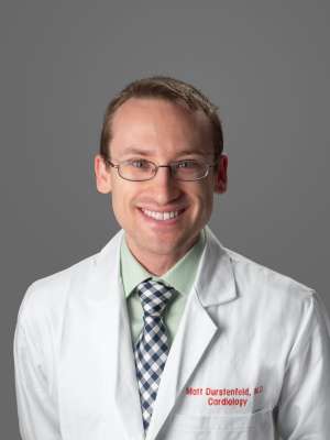 Person in white lab coat and checkered tie with face obscured