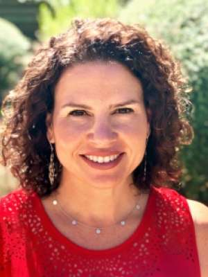 Headshot of woman with curly hair wearing red sleeveless top outdoors