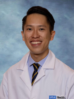 A headshot of Dr. Thang Tran who has short dark brown hair, wearing a white lab coat, tie and smiling