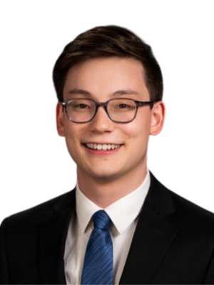 Young man wearing glasses, suit, and blue tie smiling in headshot