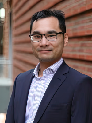 Dr. Neil Lin wearing a dark blue suit and standing against brick wall