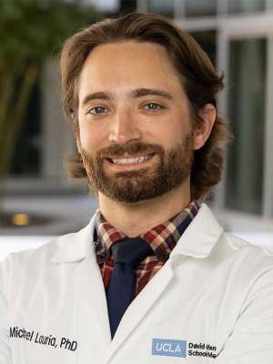 Dr. Michael Lauria posing outside, wearing a white coat and smiling.