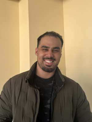 Sohaib Rafa Butt wearing a green jacket in front of a yellow wall