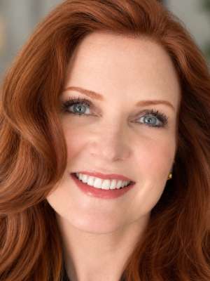 Smiling red-haired woman with blue eyes, professional headshot.
