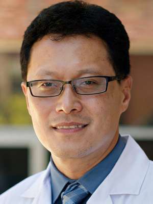 Smiling person in white coat and glasses outdoors