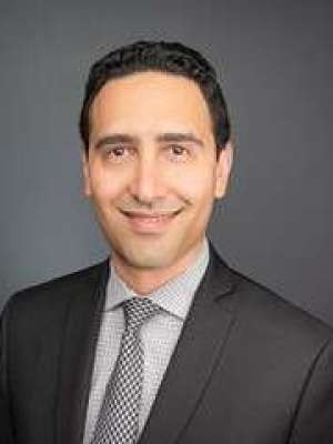 A smiling man with glasses and a grey suit.