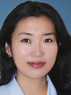 Headshot of a woman with dark hair wearing a light blue collared shirt against blue background.