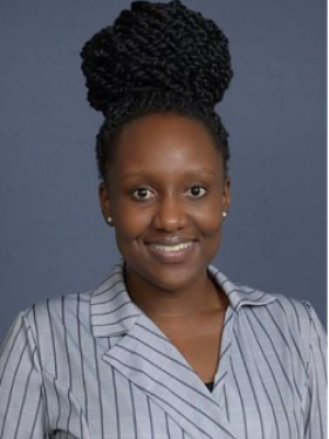 Headshot of a person with braided hair, wearing a striped shirt against a gray background.