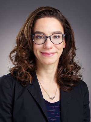 Professional headshot of woman with glasses and curly hair in a blazer