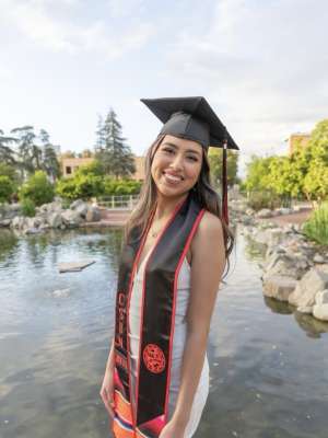Danielle wearing a white dress with a graduation cap and stole
