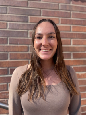 A woman with long brown hair, wearing a brown shirt, smiling in front of UCLA campus