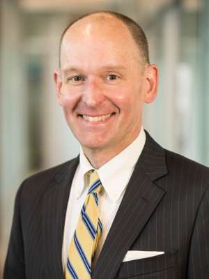 Formal portrait of a man in a suit with a striped tie against a blurred background.