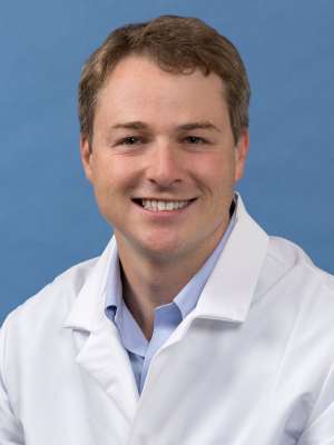 White coat head shot of Brian DeLue, smiling at the camera