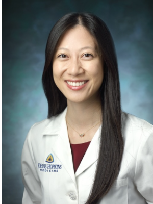 Head-and-shoulders portrait of person in white coat against teal background.