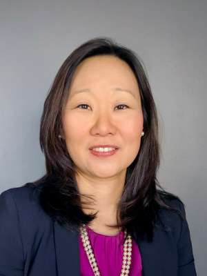 Smiling professional woman wearing blazer and necklace against gray background