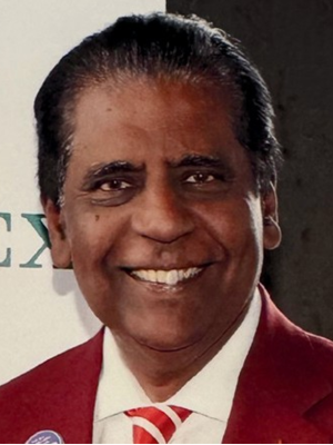 Vijay Amritraj in a red suit with a white shirt and patterned tie, standing at an event.