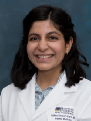 A woman with wavy black hair, wearing a resident physician's coat