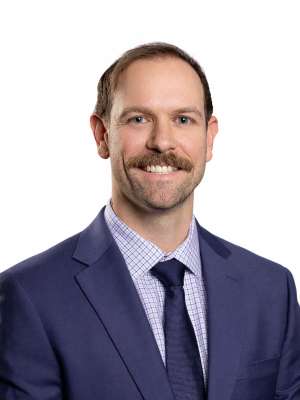 Headshot of a smiling man with mustache wearing a navy suit and tie