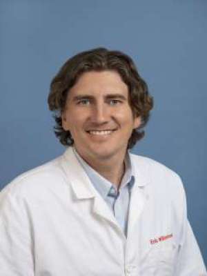 Smiling man in white lab coat against blue background.