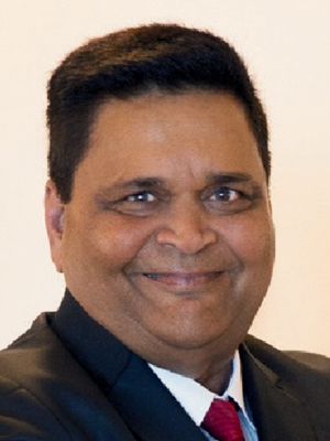 Vinod Jivrajka in a suit with a blurred face and neutral background.