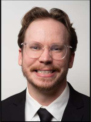 headshot of Austin Davis wearing a clear frame glasses and black suit in front of a white background