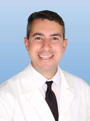 Smiling man wearing a white coat and tie on a blue background