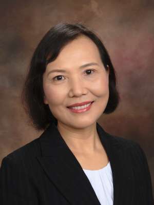 Professional headshot of person, dark blazer and white shirt, brown backdrop