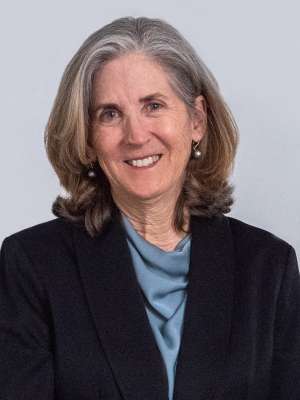 Headshot of person in dark blazer and blue blouse on light background