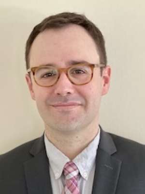 headshot of Dr. Samuel Good in black suit and pink tie