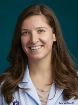 Smiling woman in white medical coat against a teal background.