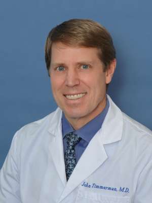 John M. Timmerman, MD wearing a white coat and tie, smiling