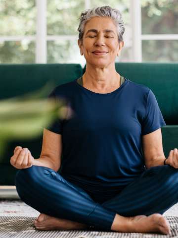 Senior woman meditating in lotus position at home.