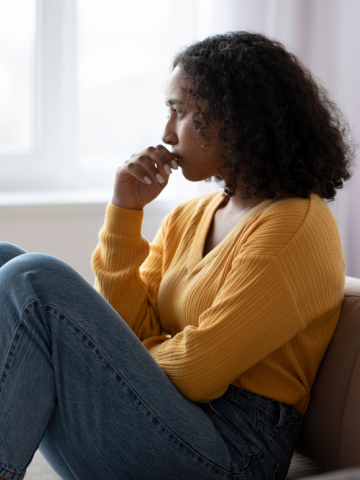 Woman sitting on a couch, appearing deep in thought.