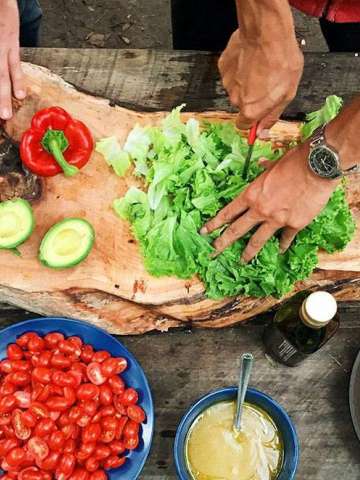 Hands preparing fresh vegetables on a wooden surface with bowls of ingredients.