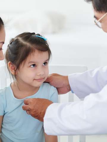 Doctor looking at his little patient while examining her with stethoscope.