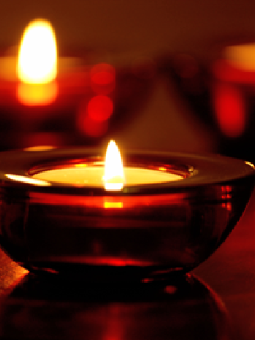 3 small Candles inside of a red glass candle holder, placed on top of a table