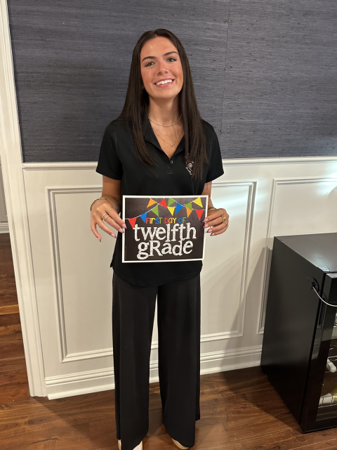 A teen girl holds up a sign indicating her first day of 12th grade.