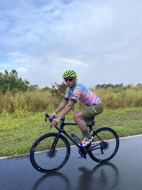 A man rides his bike on a road in Maui, with a rainbow in the background.