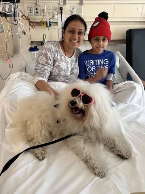 A boy, his mom and their dog relax on a hospital bed.