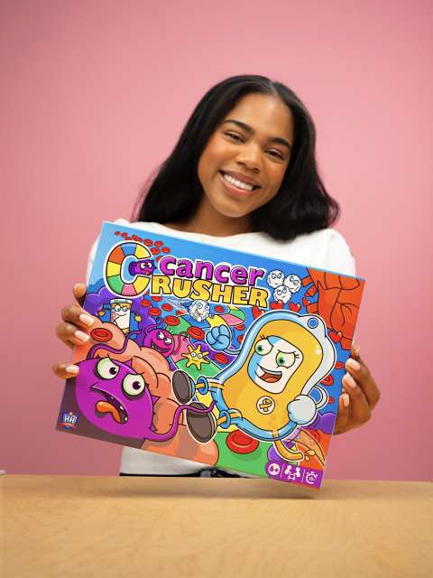 A doctor holds up the Cancer Crusher board game box.