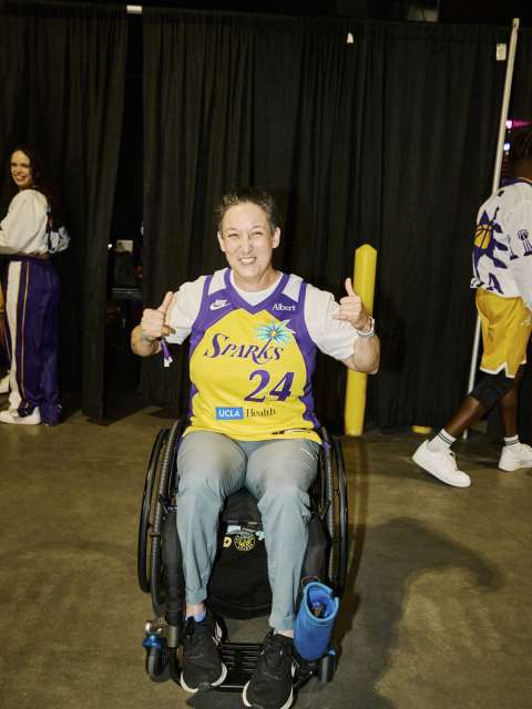 A patient in an LA Sparks jersey gives two thumbs up at the basketball game,