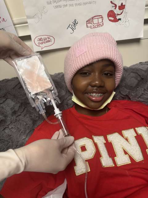 Smiling child in pink beanie and red PINK sweatshirt receiving an IV line