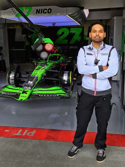 A man stands in front of a Formula 1 car at a racetrack.