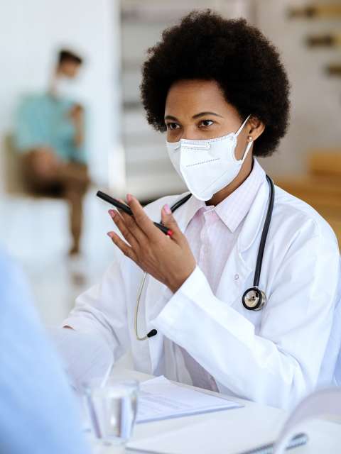 Masked Black female doctor talking to patients.