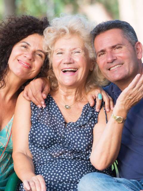 Three people smiling outdoors on a bench