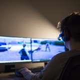 A boy plays a video game using two computer screens and a headset.