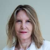 Woman wearing white medical coat facing camera, neutral background